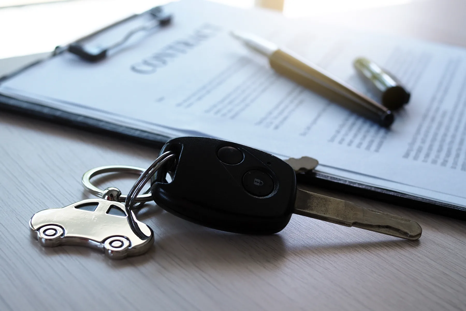 Una llave de auto sobre un contrato impreso, junto a un bolígrafo